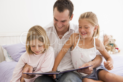 Man in bedroom with two young girls reading book and smiling