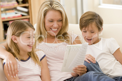 Woman and two young children in living room reading book and smi