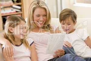 Woman and two young children in living room reading book and smi