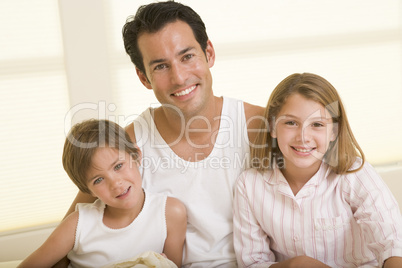 Man with two young children sitting in bed smiling