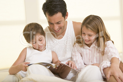 Man with two young children sitting in bed reading a book and sm