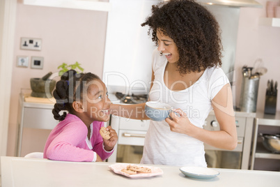 Woman and young girl in kitchen with cookies and coffee smiling