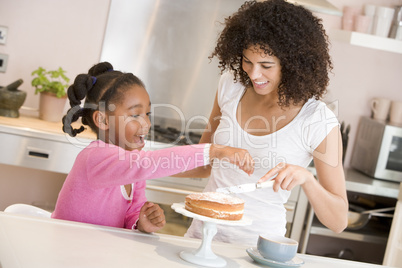 Woman and young girl in kitchen icing a cake smiling