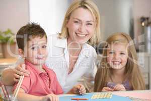 Woman and two young children in kitchen with art project smiling