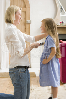 Woman in front hallway brushing young girl's hair and smiling