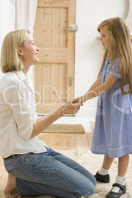 Woman in front hallway holding young girl's hands and smiling