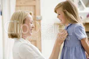 Woman in front hallway fixing young girl's dress and smiling