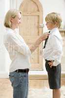 Woman in front hallway fixing young boy's tie and smiling
