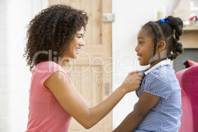 Woman in front hallway fixing young girl's dress and smiling