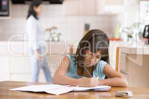 Young girl in kitchen doing homework with woman in background