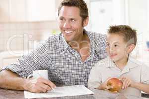 Man and young boy in kitchen with newspaper apple and coffee smi