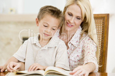 Woman and young boy reading book in dining room smiling