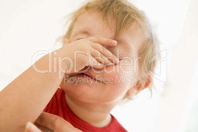 Baby indoors putting hand over face