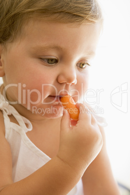 Baby indoors eating carrot.