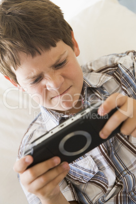 Young boy with handheld game indoors looking unhappy