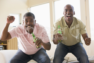 Two men in living room with beer bottles cheering and smiling