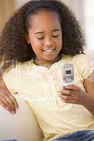 Young girl in living room using cellular phone and smiling