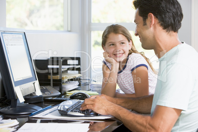 Man and young girl in home office with computer smiling