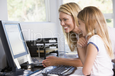 Woman and young girl in home office with computer smiling