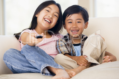 Two youngchildren in living room with remote control smiling