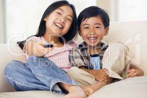 Two youngchildren in living room with remote control smiling