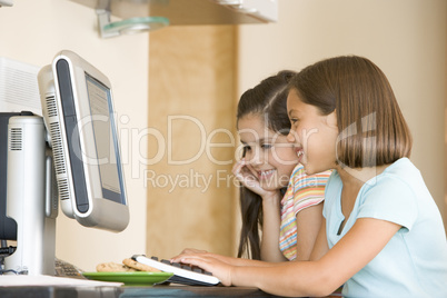 Two young girls in kitchen with computer smiling