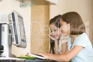 Two young girls in kitchen with computer smiling
