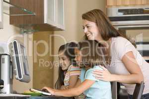 Woman and two young girls in kitchen with computer smiling