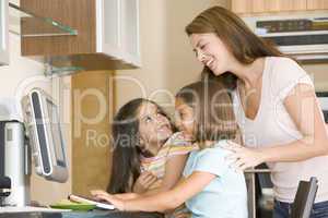 Woman and two young girls in kitchen with computer smiling
