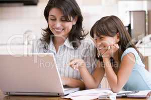 Woman and young girl in kitchen with laptop and paperwork smilin