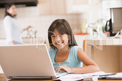 Young girl in kitchen with laptop and paperwork smiling with wom