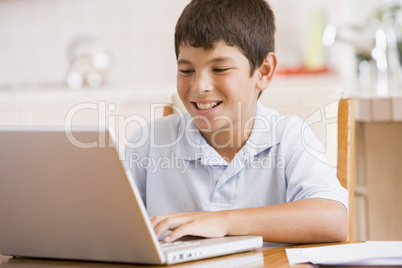 Young boy in kitchen with laptop and paperwork smiling