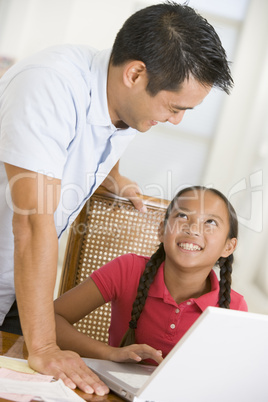Man and young girl with laptop in dining room smiling
