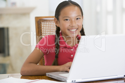 Young girl with laptop in dining room smiling