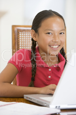 Young girl with laptop in dining room smiling