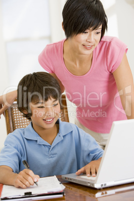 Woman helping young boy with laptop do homework in dining room s