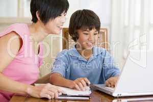 Woman helping young boy with laptop do homework in dining room s