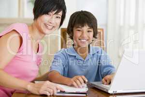 Woman helping young boy with laptop do homework in dining room s