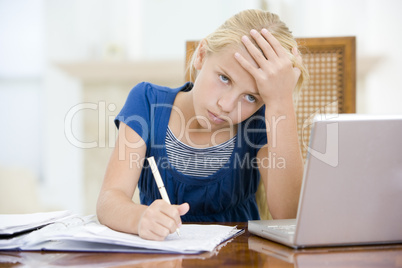 Young girl with laptop doing homework in dining room looking unh
