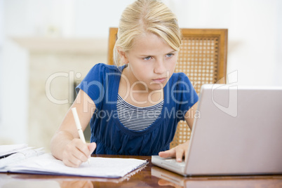 Young girl with laptop doing homework in dining room