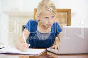 Young girl with laptop doing homework in dining room