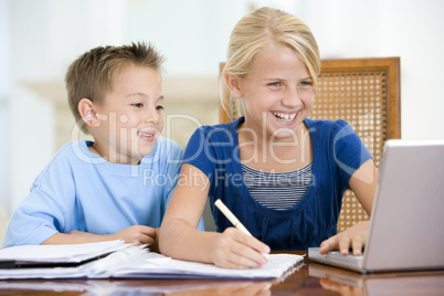 Two young children with laptop doing homework in dining room smi