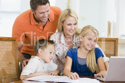 Couple helping two young children with laptop do homework in din