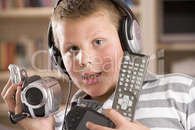 Young boy wearing headphones in bedroom holding many electronic