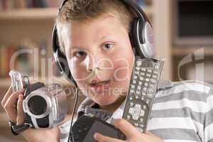 Young boy wearing headphones in bedroom holding many electronic