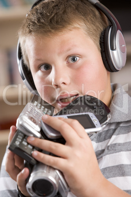Young boy wearing headphones in bedroom holding many electronic