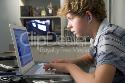 Young boy in bedroom using laptop and listening to MP3 player