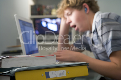 Young boy in bedroom yawning using laptop and listening to MP3 p