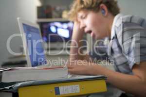 Young boy in bedroom yawning using laptop and listening to MP3 p