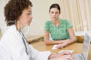 Doctor using laptop with woman in doctor's office frowning